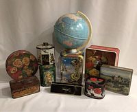 Photo showing nine vintage collectible tins and a vintage globe on stand arranged on flat surface.