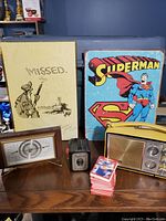 Wide shot showing all items including radio, barometer, camera, Superman sign, hunting sign, and cards