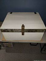 Front view of the white wooden chest with metal bands and latch.