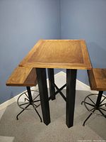 Bar table with oak top and black legs, flanked by two oak seat stools with black metal bases