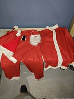Santa Claus costume laid out on a table including jacket, pants, black belt, and white beard.
