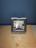 Front view of gray stretch couch slip cover in original packaging on wooden surface against blue background.