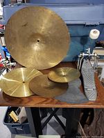 Image showing five cymbals of various sizes arranged on a table along with a drum kick pedal.