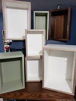 Six assorted decorative rectangular boxes displayed upright showing size and color variations including white with wood frame accents, green, and dark brown.