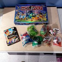 Full lot including Disney Monopoly game, Bambi DVD, and seven sealed Disney character figurines on a table.