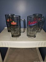 Four extra large glass beer mugs with two featuring the Sleeman logo and two featuring Boston's The Gourmet Pizza logo.