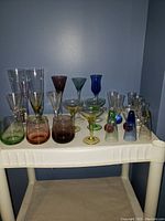 Wide view of full assortment of colored glassware on plastic shelf against gray wall.