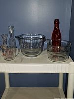 Overview of all items showing two measuring cups, two mixing bowls, red glass bottle, and two small glass decanters.
