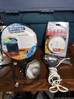 Photo showing the fire alarm still in original packaging, flood light, hair dryer, and the round car wash kit on wooden surface