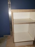Photo showing the front open shelves of the white nightstand with plywood edges and a ruler for scale indicating shelf height.