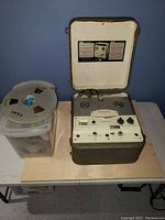Webcor Regent reel to reel tape recorder with multiple reels of tape beside it on a wooden table.