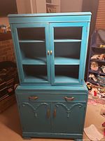 Front view of aqua blue wooden cabinet with two doors on top (missing glass) and two drawers and doors at bottom