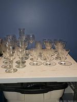 Overview of assorted wine glasses including tall and short stemmed variations on white table against blue wall.