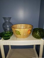 Front view of wooden bowl with peach, leaf, and orange painted images on the front side, alongside various glassware items including clear vase, green bowl, and textured green vase.