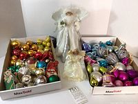 Photo showing two angel tree toppers with ceramic faces and two large boxes filled with assorted Christmas ornaments in various colors and styles, highlighting the condition and variety