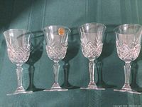 Set of four clear stemmed wine glasses with intricate cut crystal patterns on the bowl. One glass shows the original Cristal Arques authenticity sticker.