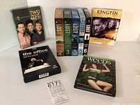 Photo showing boxed DVD sets including Two and a Half Men season 8, The Office series 1 and 2, Kingpin producer's cut, Weeds season 5, and LOST seasons 2 to 6 stacked to the side.