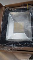 View of the LED Flood Light front showing LED array and reflector behind clear plastic wrap in box.