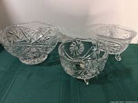 Three crystal bowls displayed on a green surface, showing bowl sizes and designs