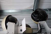 Three dome security cameras on a shelf, one with a damaged dome cover showing internal wiring and cracked black plastic.