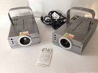 Front view showing two metal Dynamix laser show systems with carry handles, power cables, and front lens.