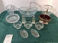 Overview of vintage crystal and cut glass items displayed on green fabric background. Includes handled basket, footed bowl, salt and pepper shakers, small dishes, and ashtray.