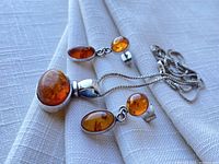 Overview of amber pendant necklace and matching amber drop earrings with sterling silver settings, laid on white fabric.