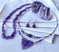 Photo showing the 18 inch necklace, amethyst pendant necklace, earrings, and two raw amethyst stones arranged on cloth.