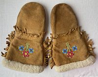 Front view of both mittens showing beadwork floral design, fringe, and sheepskin cuff lining.