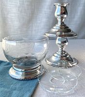 Etched glass grapes dish with sterling base next to a sterling candle holder and two glass bobeche on blue fabric.