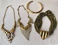 Three brass costume jewelry pieces on cream fabric: two necklaces and one choker bracelet.