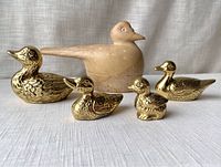 Group photo showing four solid brass duck figurines and one beige stone covered keepsake duck.