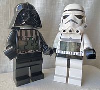Front view of both Lego Star Wars Darth Vader and Stormtrooper alarm clocks standing side by side showing digital time displays.