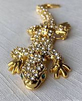 Close-up top view of the rhinestone encrusted gold-tone lizard salamander brooch showing green eyes.