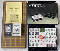 The Game of Go board with black and white stones in their boxes alongside the yellow instruction booklet; Mahjong set box with case and tiles visible inside.