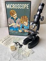 Complete microscope with box, instruction sheet, glass slides, cover glass, and specimen containers arranged on table