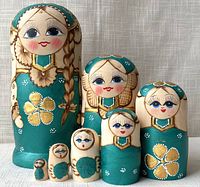 Front view of all seven nesting dolls arranged largest to smallest, showing detailed facial features, braided hair on the largest, and teal/gold painted designs