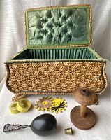 Woven sewing box exterior showing lid open, tufted lining, and contents: wooden spool, darner, measuring tapes, thread keepers, thimble.