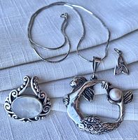 Necklace chain with three pendants displayed on fabric, showing overall lot contents