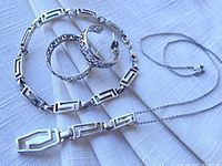 Photo showing the full set of sterling silver necklace, bracelet, and earrings laid on white fabric.