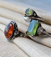 Close-up of three rings highlighting amber cabochon, large rectangular green stone, and smaller green round stone