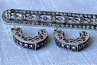 Close-up showing an elongated rectangular sterling silver brooch decorated with marcasite and leaf motif, alongside a pair of half-hoop sterling silver earrings with marcasite and filigree detailing.