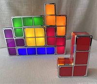 Front view showing five stacked Tetris LED nightlight blocks in red, orange, yellow, green, blue, and purple glowing brightly and one separate red block.