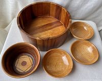 Set of five wood bowls arranged together including one large wood bowl, one inlaid wood bowl with geometric pattern, and three smaller polished wooden serving bowls.