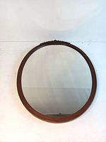 Front view of oval wood framed mirror showing the entire mirrored surface and wooden frame with carved decorative detail at top.