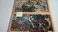 Wide angle photo showing assortment of colorful costume jewelry piled in wooden tray compartments. Varied styles and colors visible.