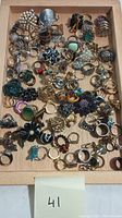 Overview of costume jewelry rings in diverse styles and colors arranged on a wooden tray.