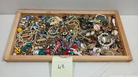 Wide view of costume jewelry lot arranged loosely on a wooden tray showing diverse types and colors of pieces