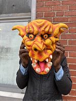 Front view of the rubber plush demon face wall hanging held up in front of a person.