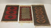 Three hand knotted Indo Bokhara rugs displayed flat on table showing patterns and fringe edges